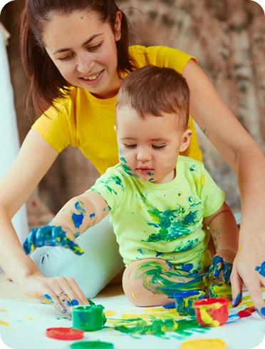 Adult helping a young child paint with colourful handprints